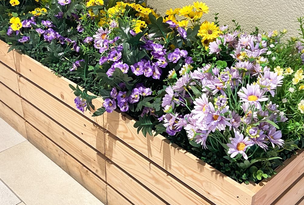 Wooden raised planter filled with colourful blooming flowers in a garden setting.